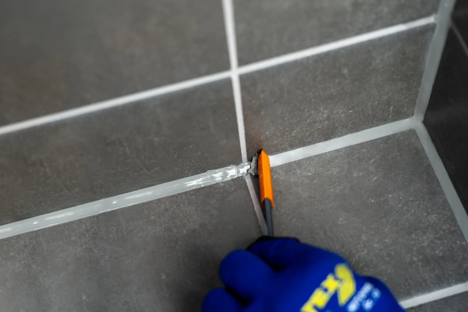 Altes Silikon wird mit dem Fugenmesser aus der Ecke zwischen zwei Fliesenflächen gezogen